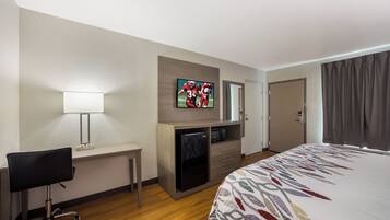 A hotel room with a bed, desk, chair, television, and a door.