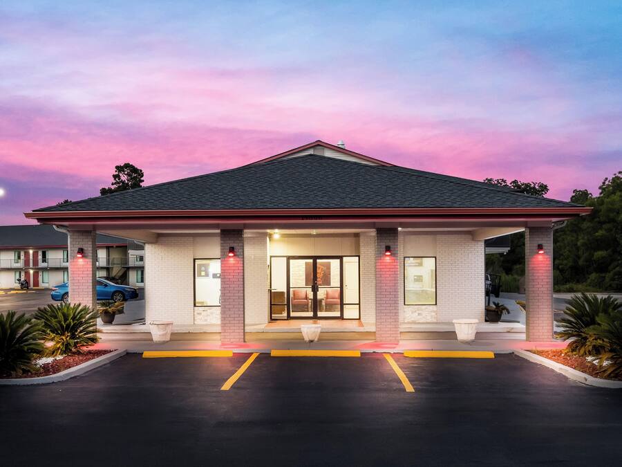 Um motel com estrutura de um andar, teto plano e estacionamento com vagas demarcadas.