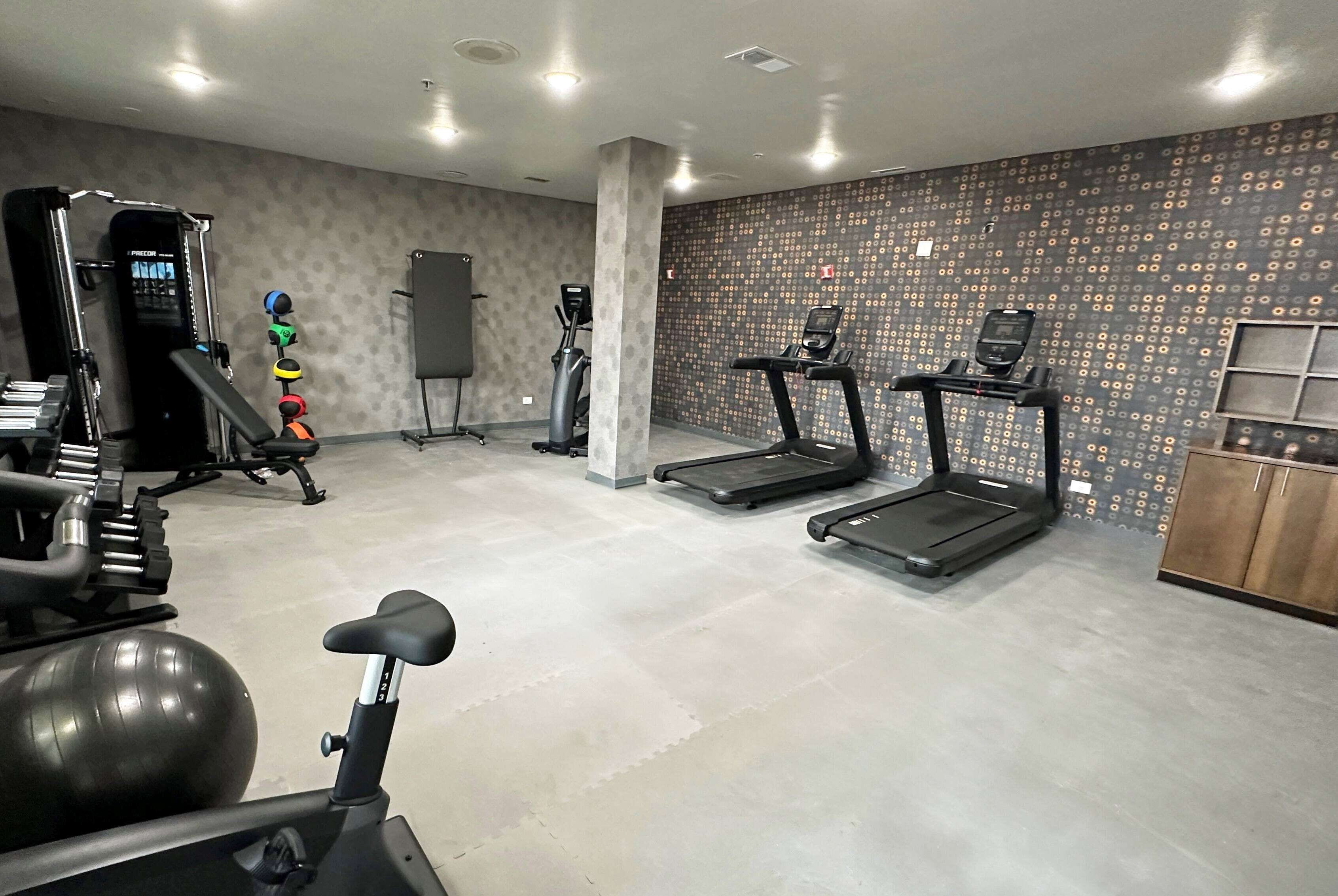 A gym with exercise equipment including a treadmill, elliptical, and weight machines.