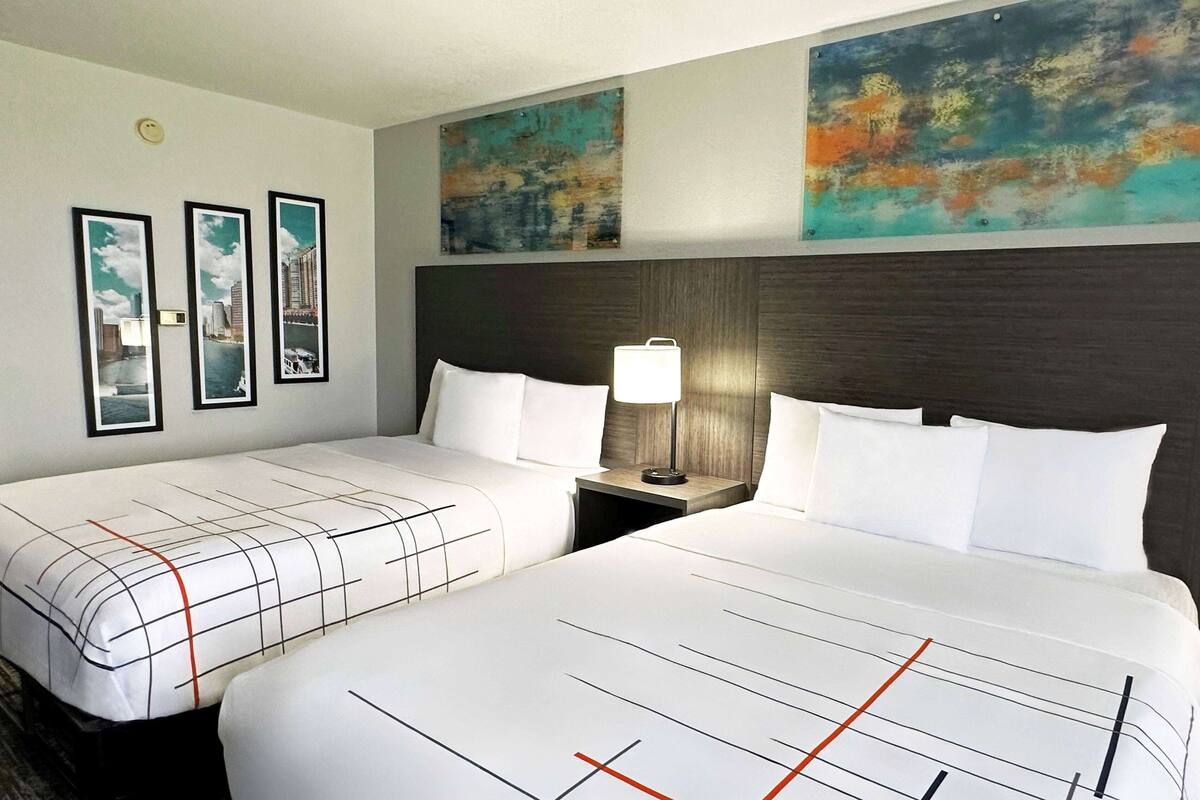 Une chambre d’hôtel avec deux lits, une table de chevet avec une lampe et trois tableaux encadrés accrochés au mur.