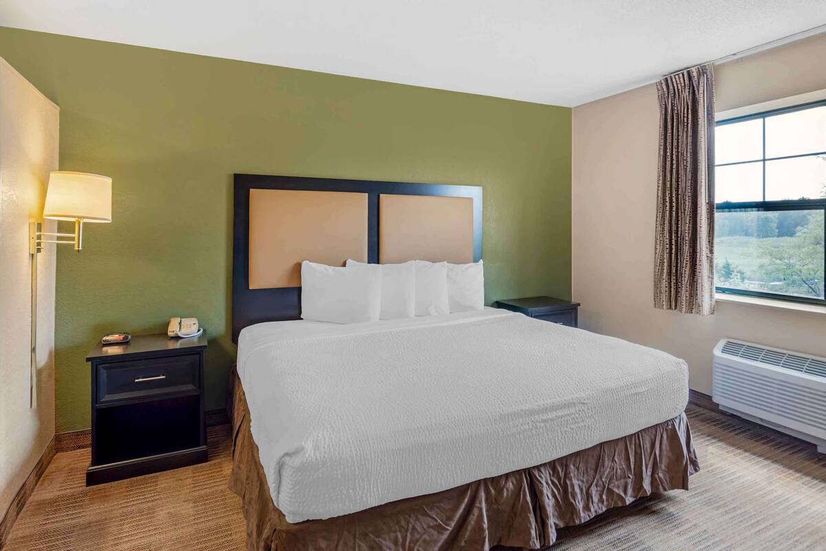 A hotel room with a large bed, a nightstand, a lamp, and a window with curtains.