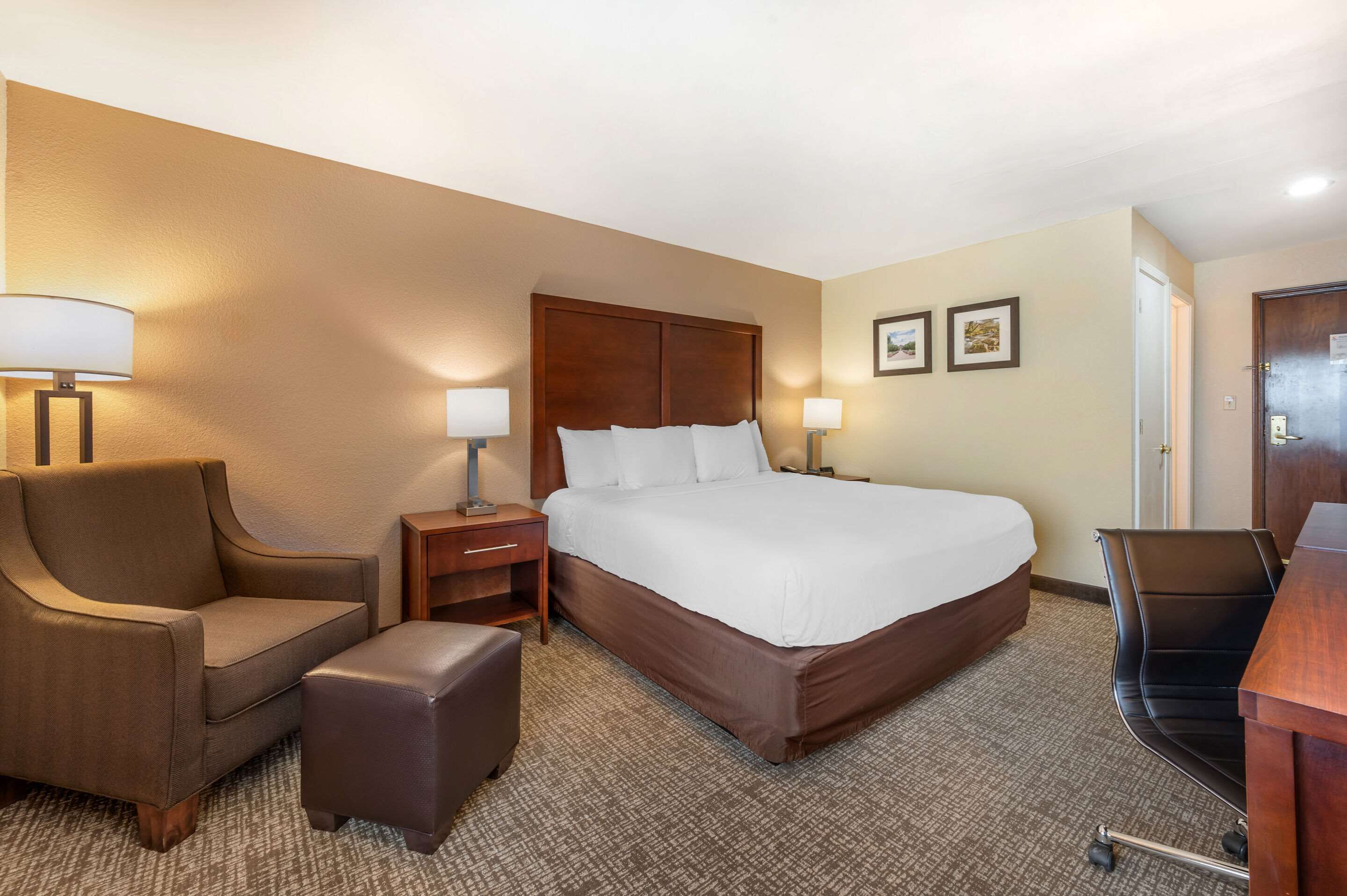 A hotel room with a large bed, a desk, a chair, a nightstand, and two wall-mounted lamps.