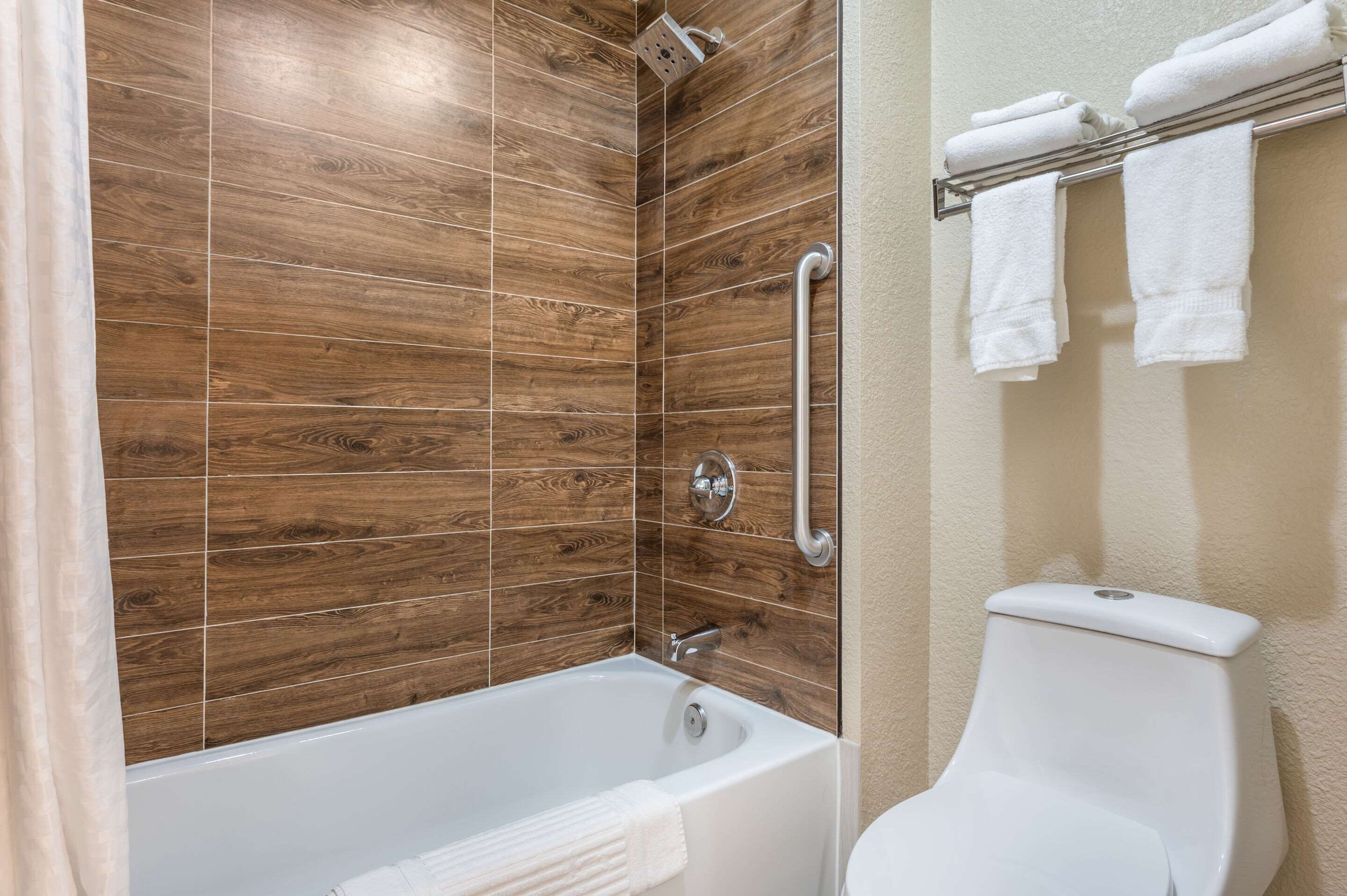 A bathroom with a wooden-tiled shower wall, a white bathtub, and a toilet with a towel rack.