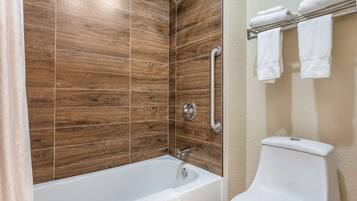 A bathroom with a wooden-tiled shower wall, a white bathtub, and a toilet with a towel rack.
