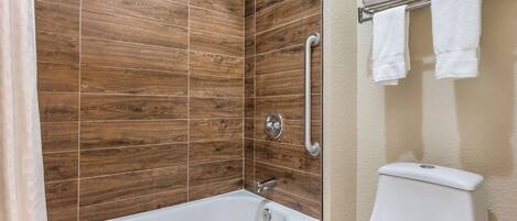 Un baño con pared de ducha de azulejos de madera, una bañera blanca y un inodoro con toallero.