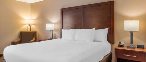 A hotel room with a large bed, two bedside tables with lamps, a chair, and a nightstand with a phone and a digital clock.
