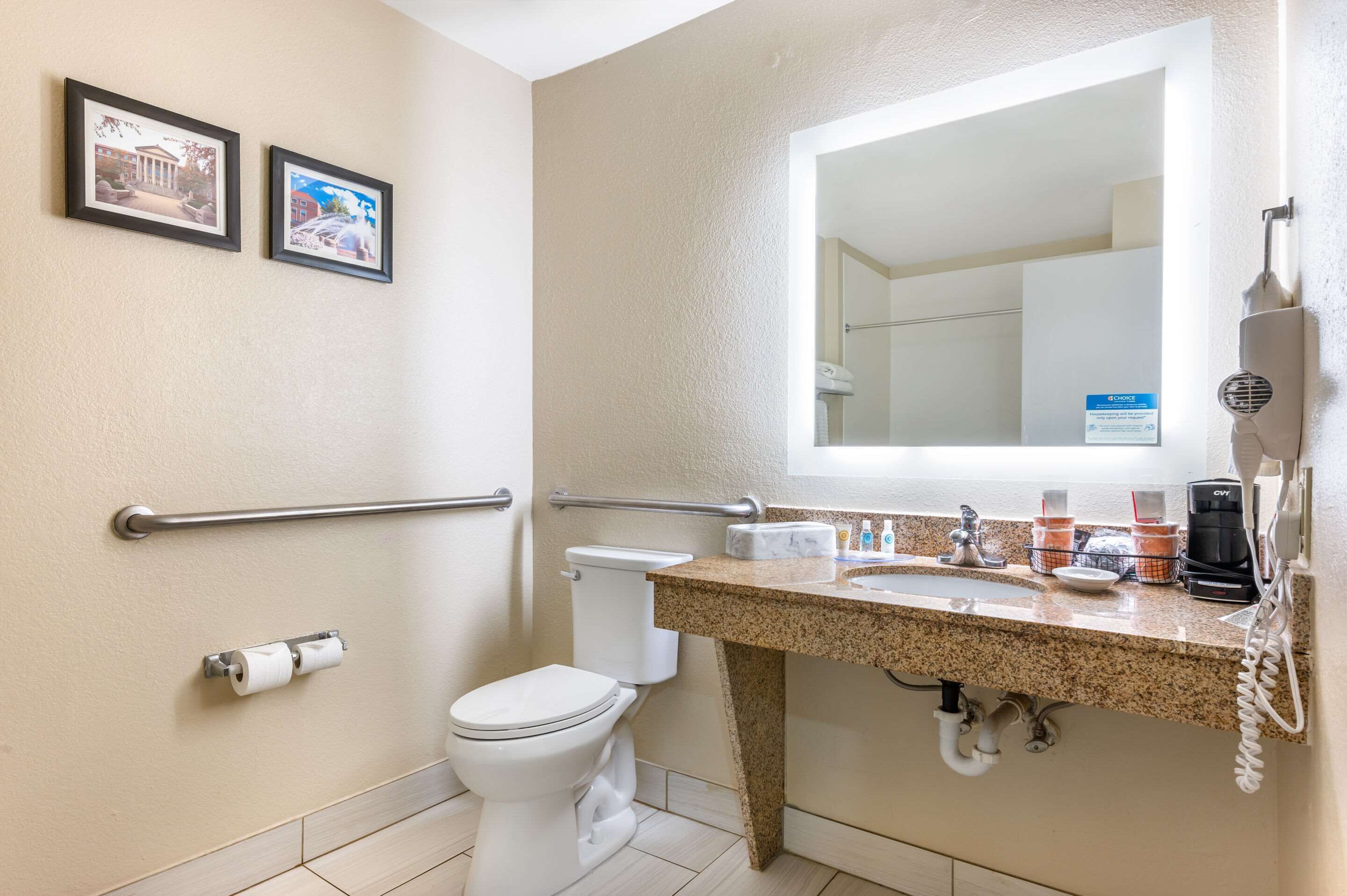 Un baño con inodoro, lavamanos con espejo y dos cuadros en la pared.