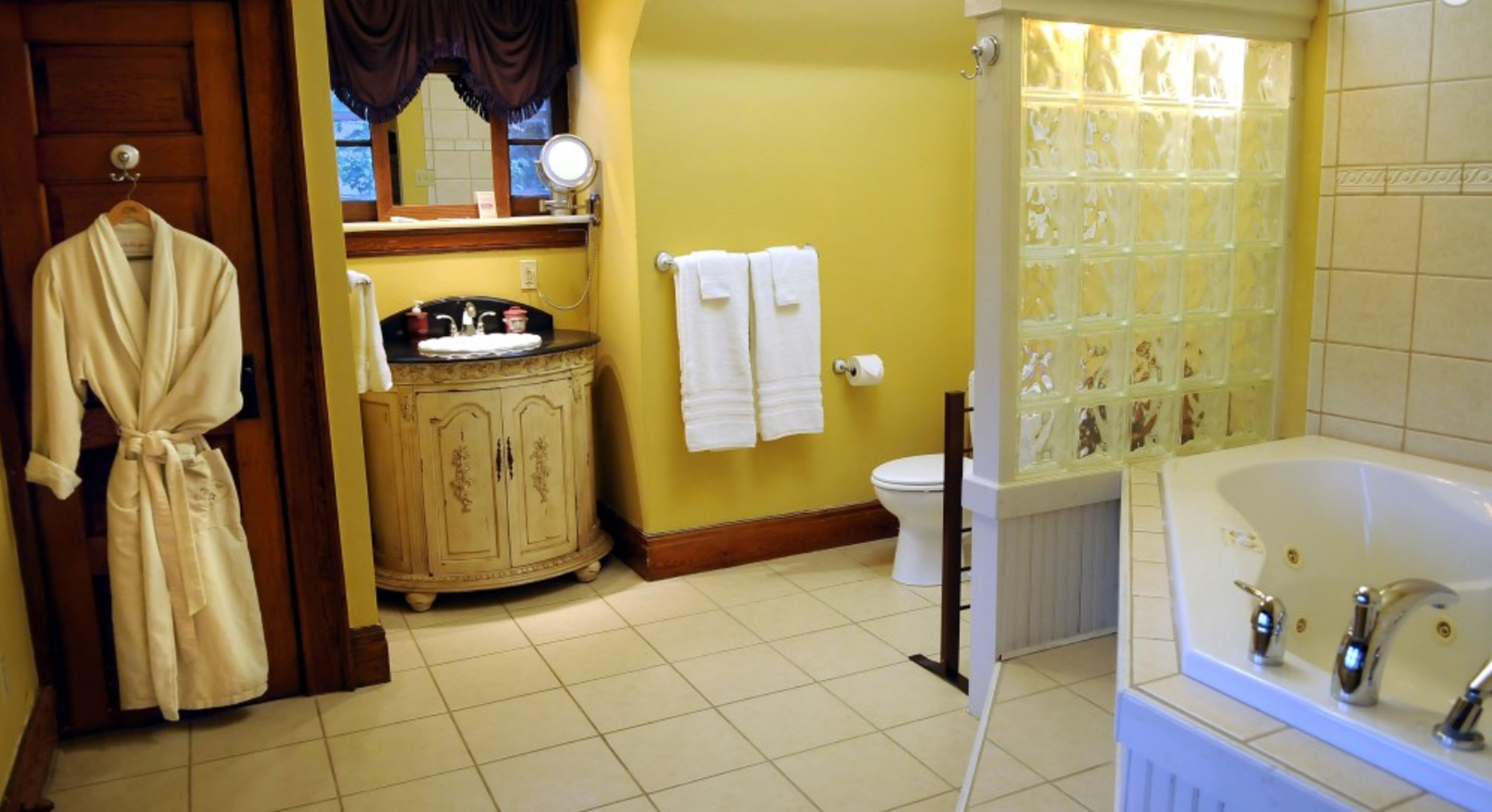 Un baño con bañera, inodoro, tocador y una bata colgada junto a la puerta.