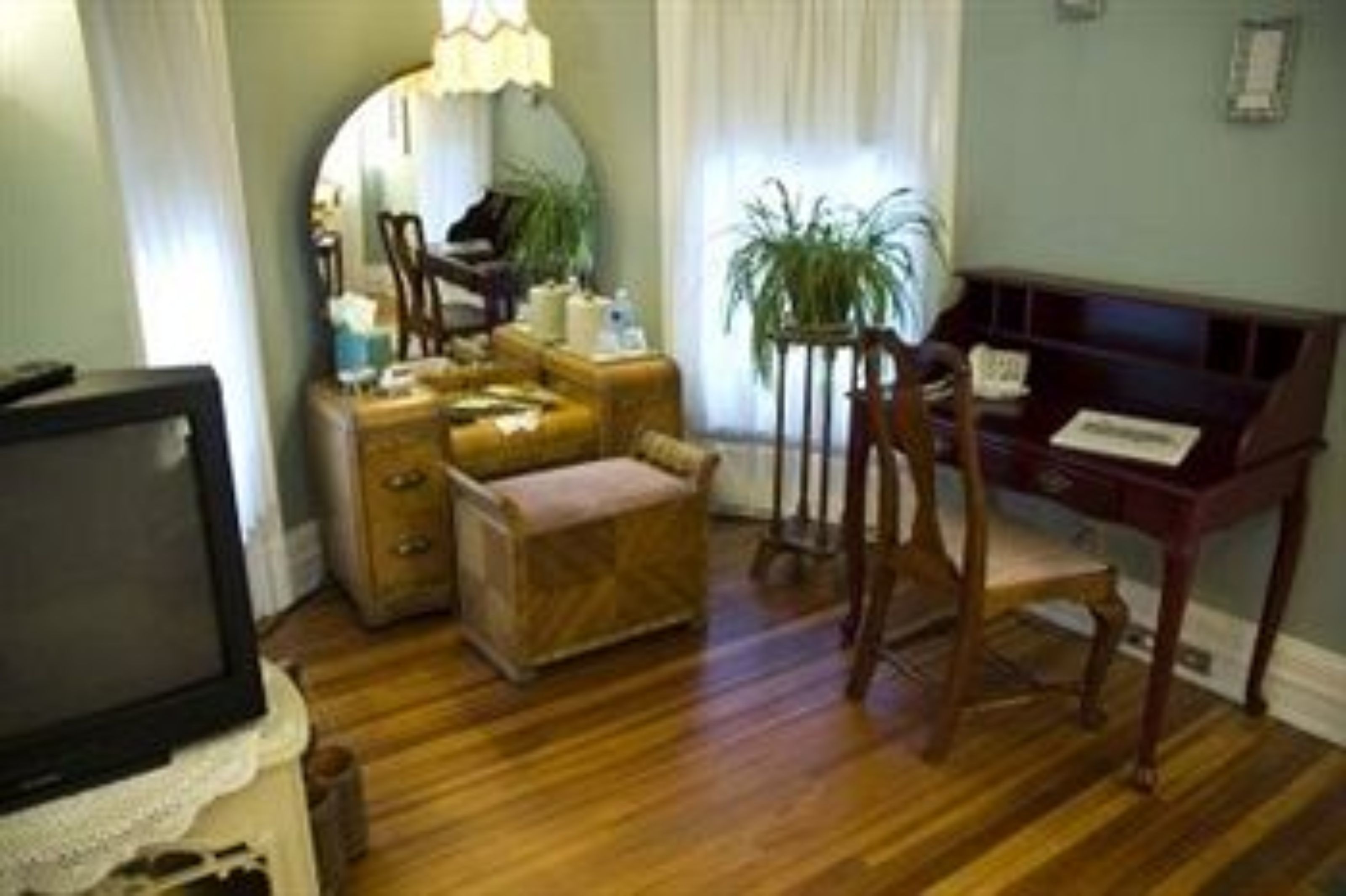 Una habitación con piso de madera, un escritorio con lámpara, una silla, una mesita y un televisor.