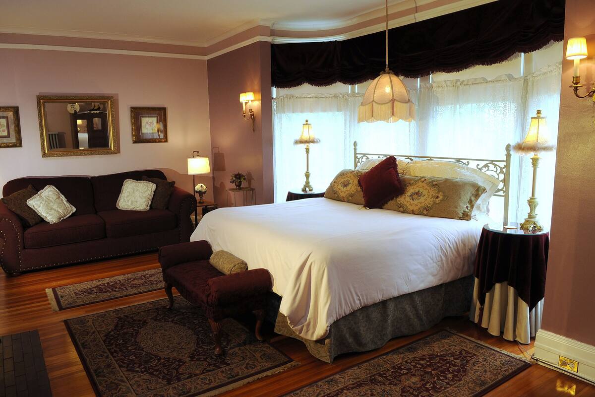 A bedroom with a large bed, a sitting area with a sofa, and two side tables with lamps.