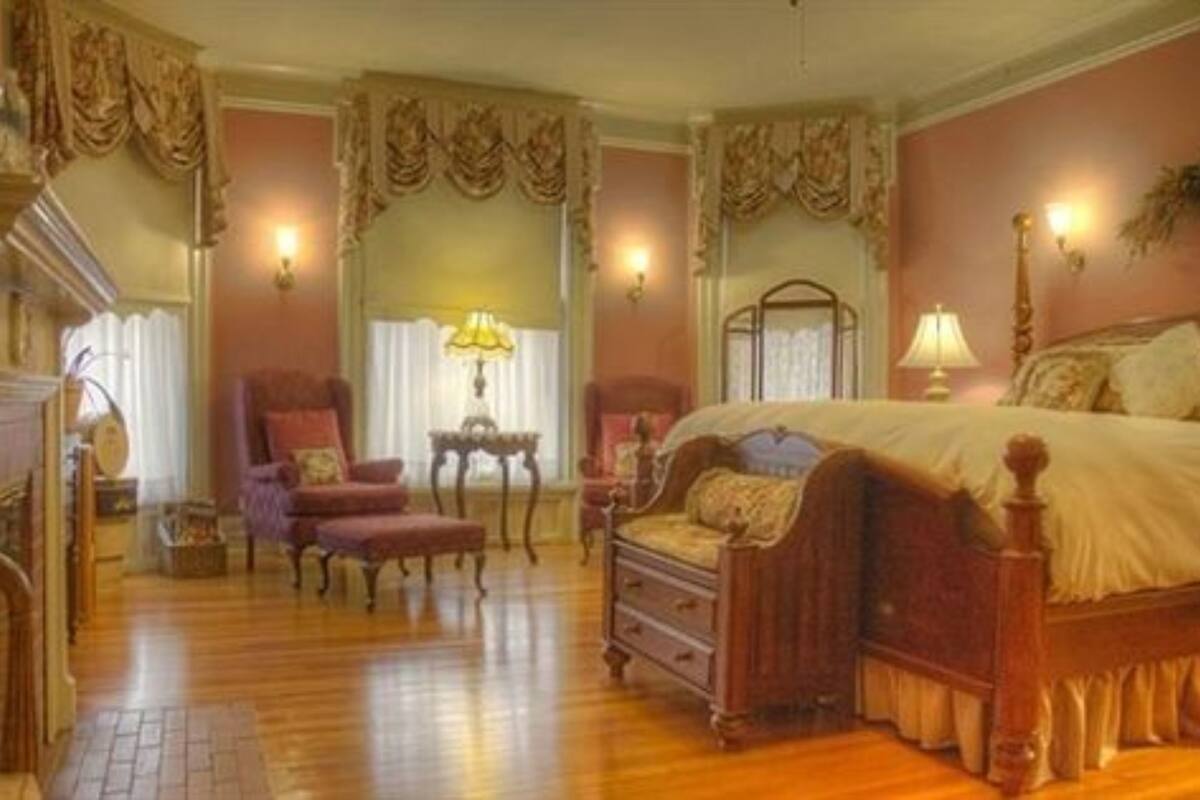 A traditional bedroom with a wooden floor, a four-poster bed, a chair, a nightstand, and a lamp.