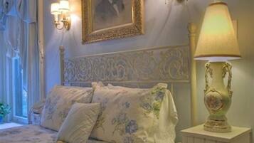 Un dormitorio con una cama, ropa de cama estampada con motivos florales, una lámpara decorativa y un cuadro en la pared.