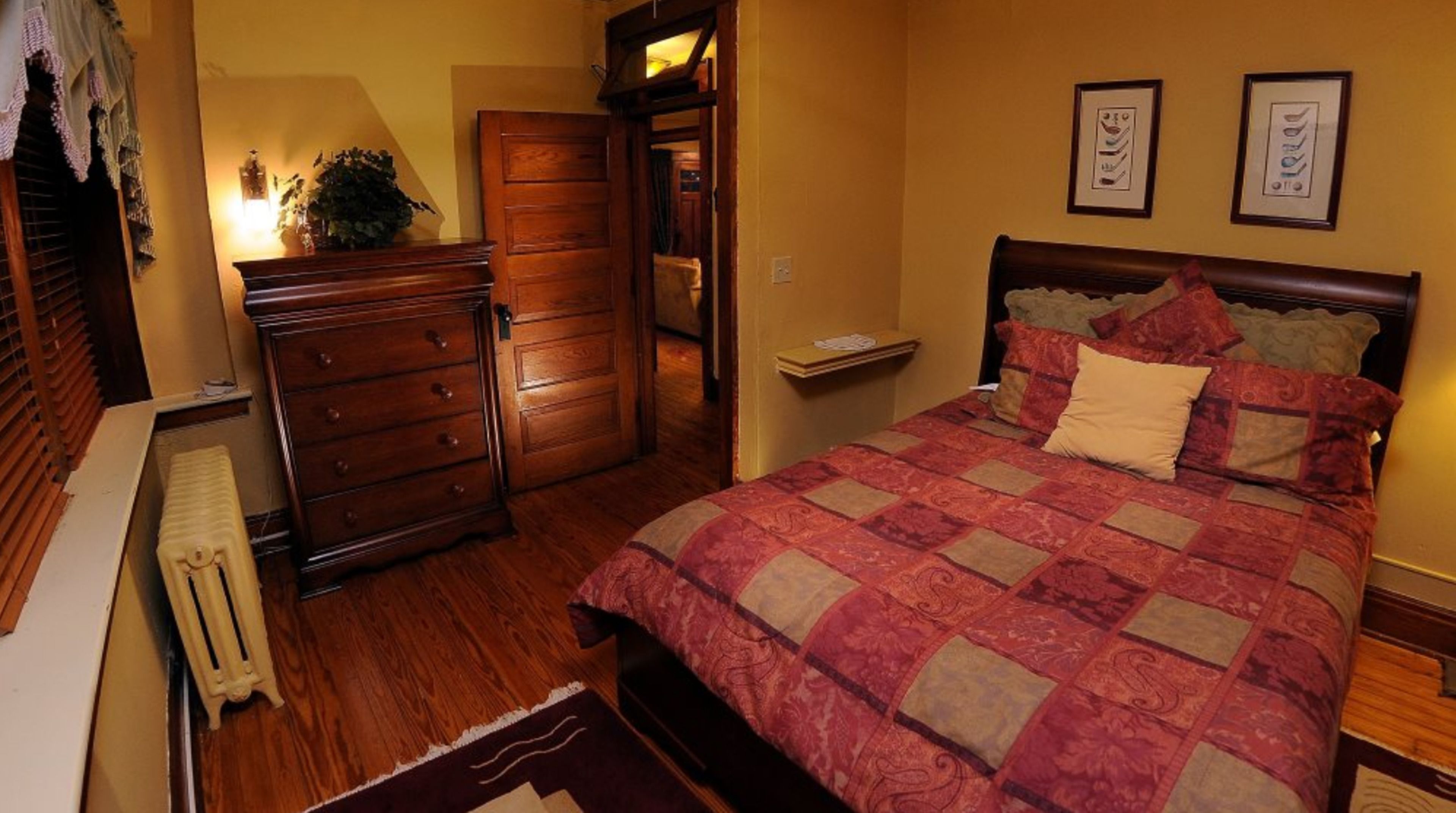 Un dormitorio con un aparador de madera, una cama con colcha estampada y un radiador.