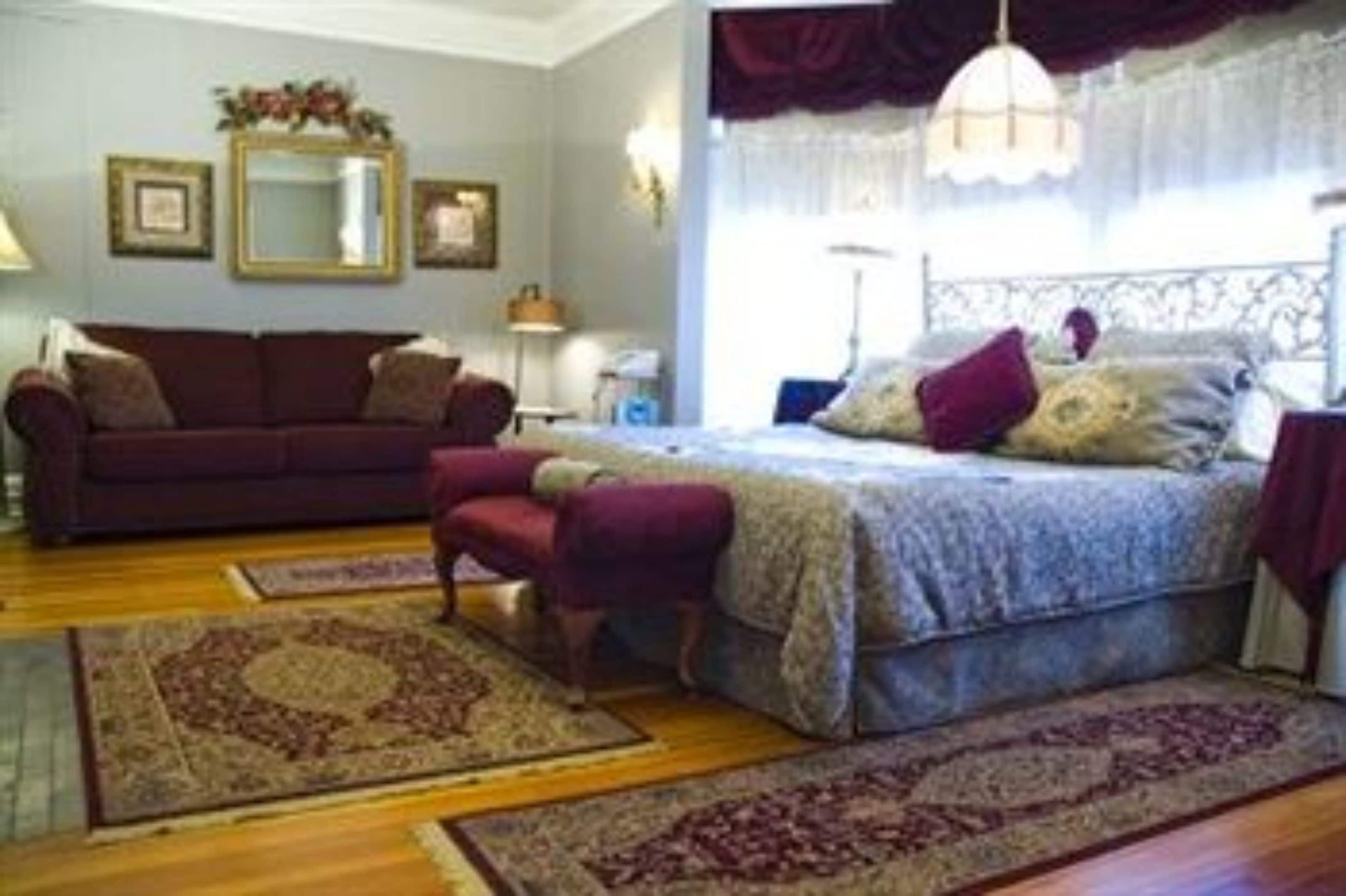 Un dormitorio con cama, sofá y sillón. Hay dos alfombras en el suelo.