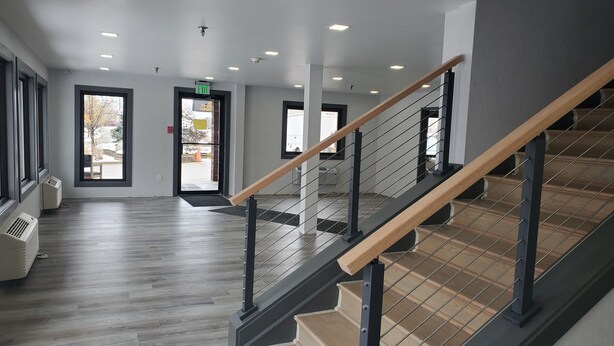 Un intérieur moderne avec un escalier en bois, un grand espace ouvert et de nombreuses portes donnant sur l’extérieur.