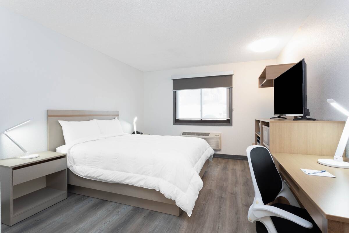 Habitación de hotel con cama, escritorio, silla, televisor y ventana.