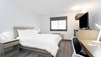 Habitación de hotel con cama, escritorio, silla, televisor y ventana.