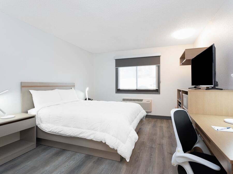 A hotel room with a bed, desk, chair, TV, and a window.
