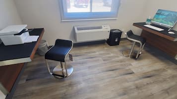 A modern office with two black chairs, a desk with a printer, a computer, and an air conditioning unit.