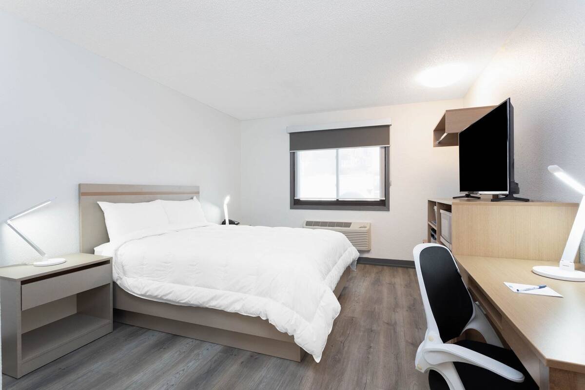 Una habitación de hotel moderna con cama, escritorio, silla, televisión y ventana.