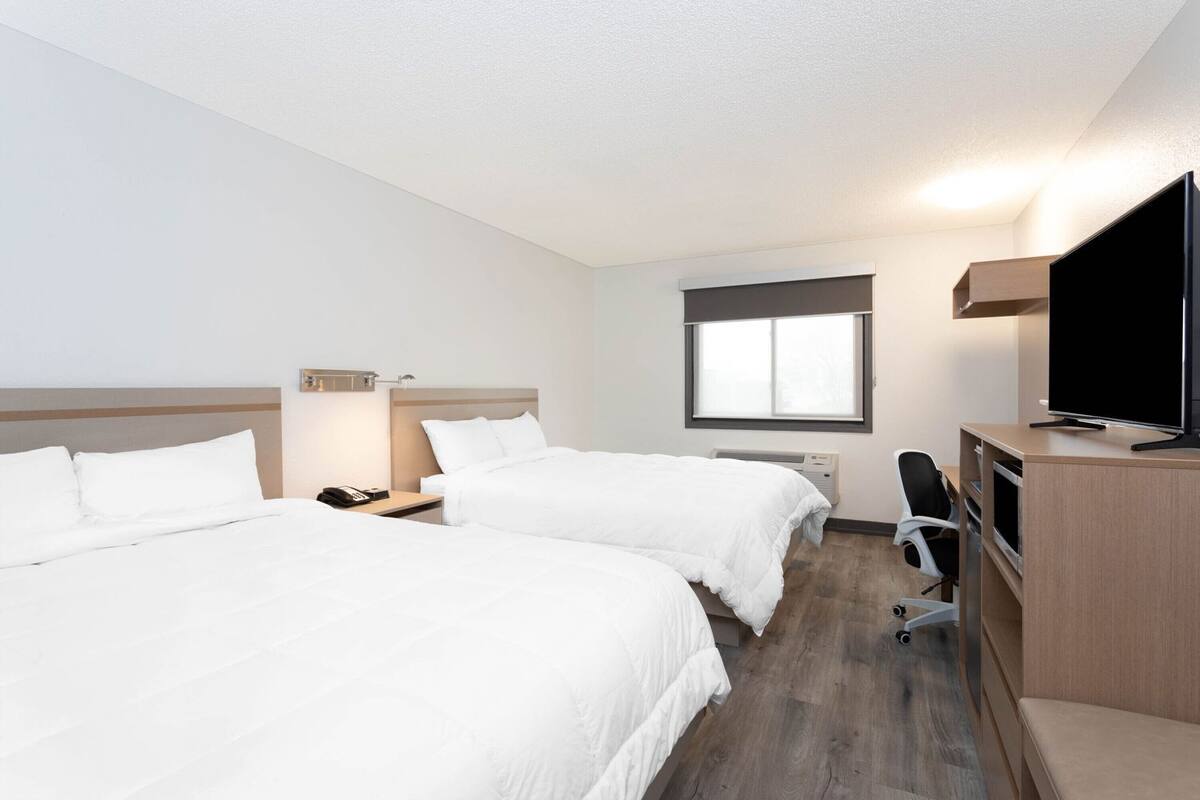 Habitación de hotel con dos camas, un escritorio, televisor de pantalla plana, una silla y una ventana.