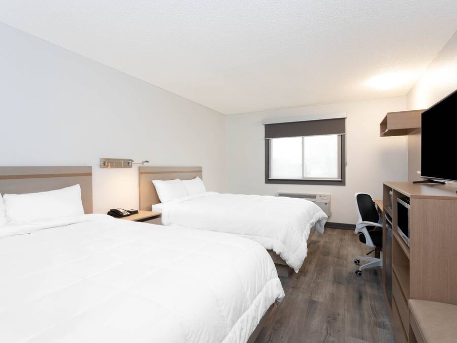 A hotel room with two beds, a desk, a chair, a TV, and a window.