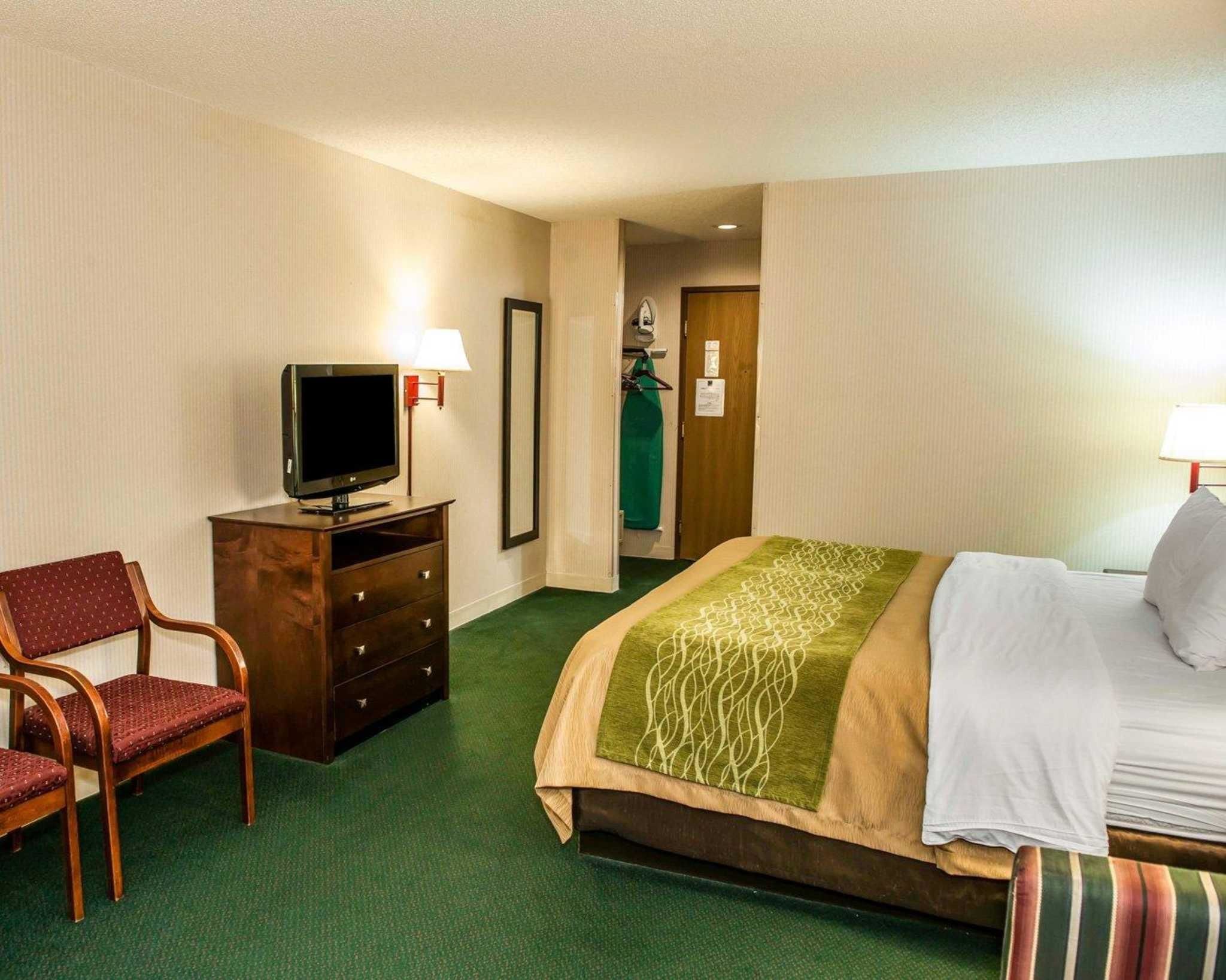 Une chambre d’hôtel avec un lit, un téléviseur posé sur une commode, une chaise et une porte donnant sur un couloir.