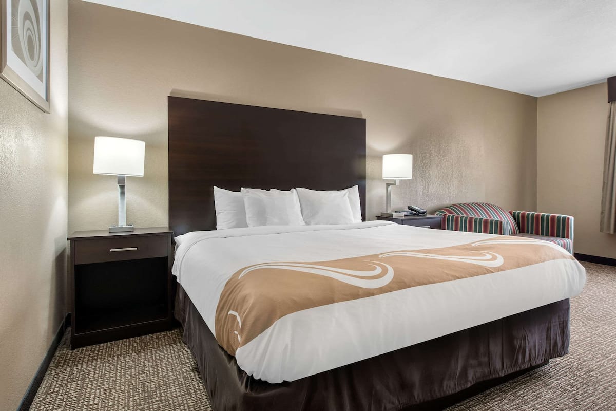 A hotel room with a large bed, two bedside tables, a headboard, and a striped couch.