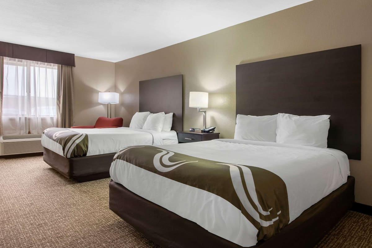 A hotel room with two beds, a desk, a chair, and a large window with curtains.