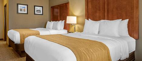 A hotel room with two beds, a wooden headboard, a lamp, and two framed pictures on the wall.