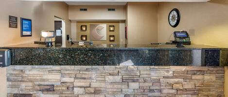 A reception area with a stone wall, a clock, and a desk with a computer and a phone.
