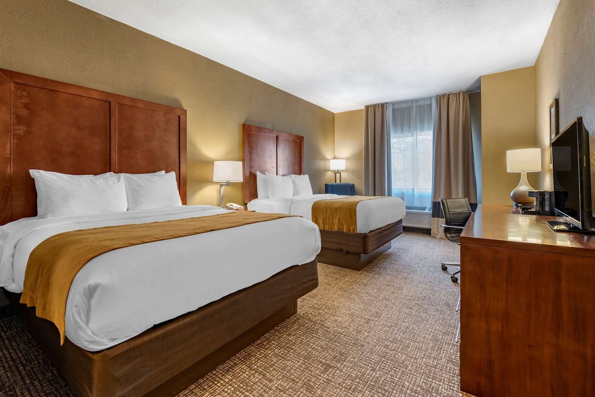 A hotel room with two beds, a desk, a chair, and a television.
