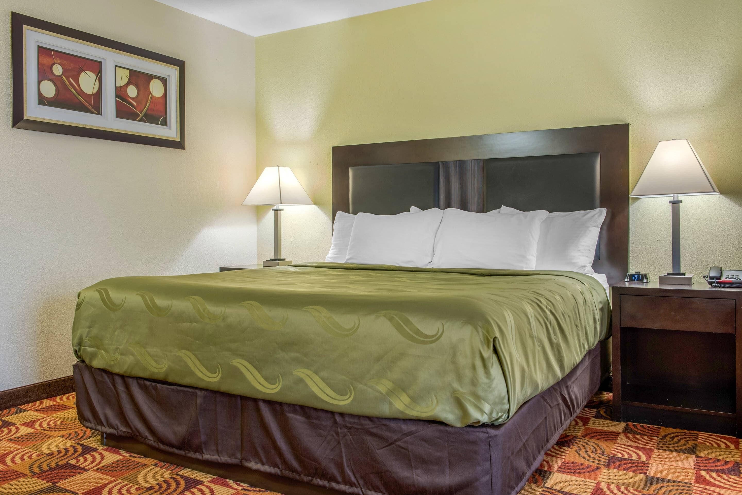 A hotel room with a bed, two bedside lamps, a nightstand, and a framed picture on the wall.