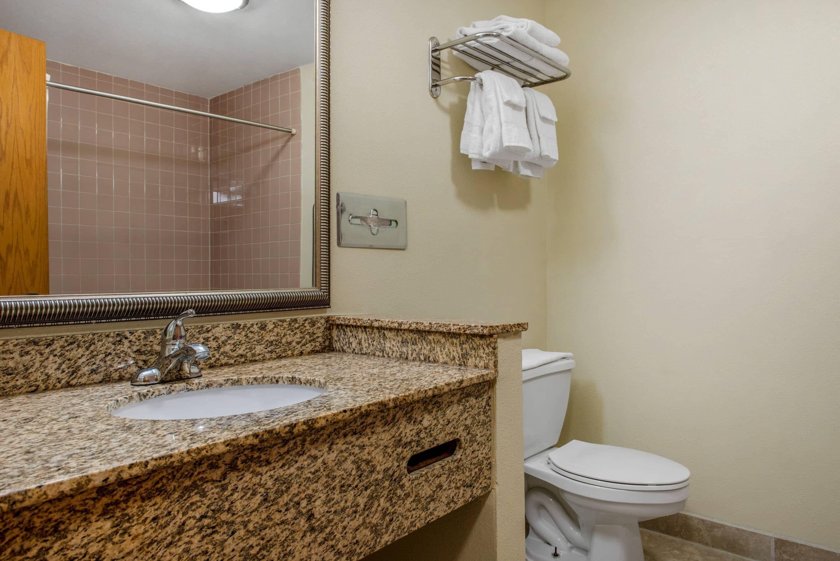 A bathroom with a granite countertop sink, a mirror, a towel rack, and a toilet.