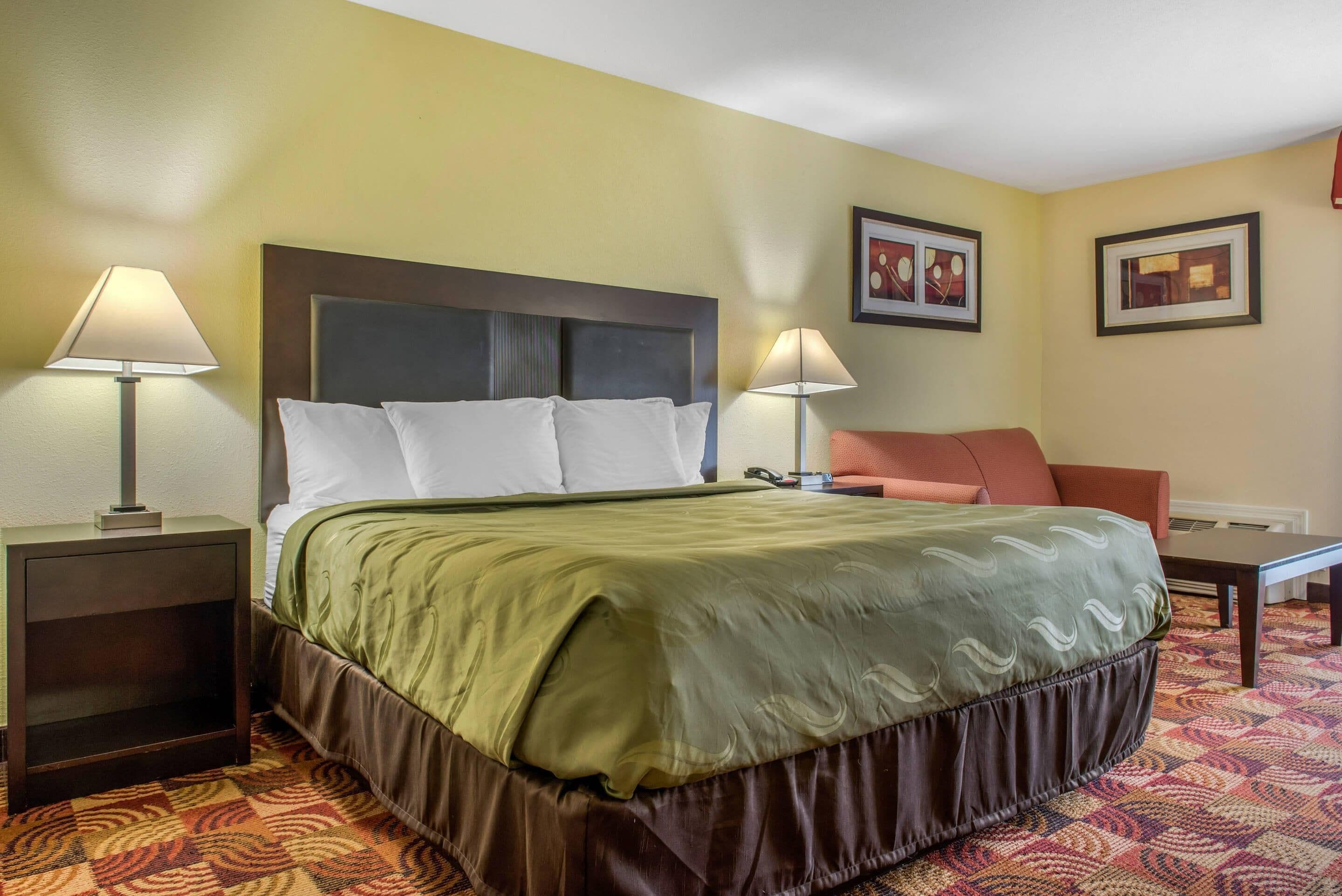 A hotel room with a bed, two bedside lamps, a nightstand, a chair, and two framed pictures on the wall.