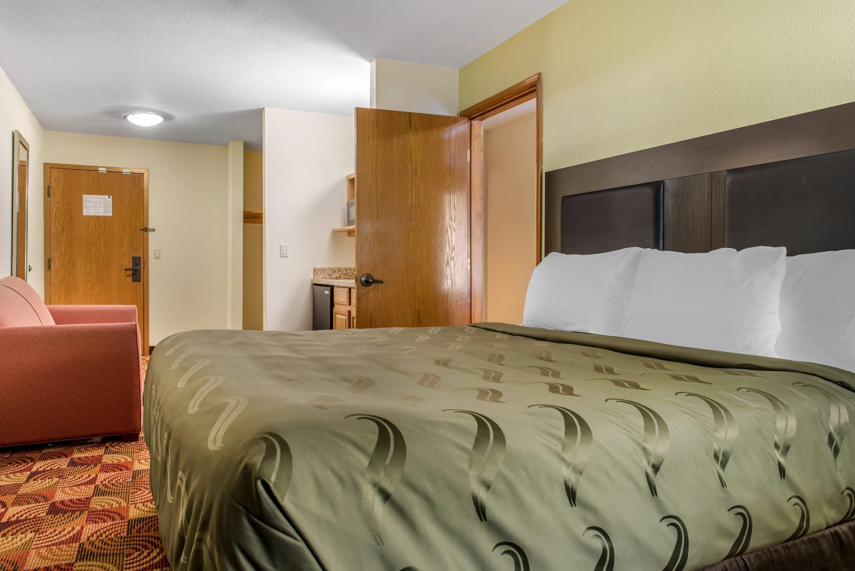 A hotel room with a bed, a chair, a wooden door, and a small table.