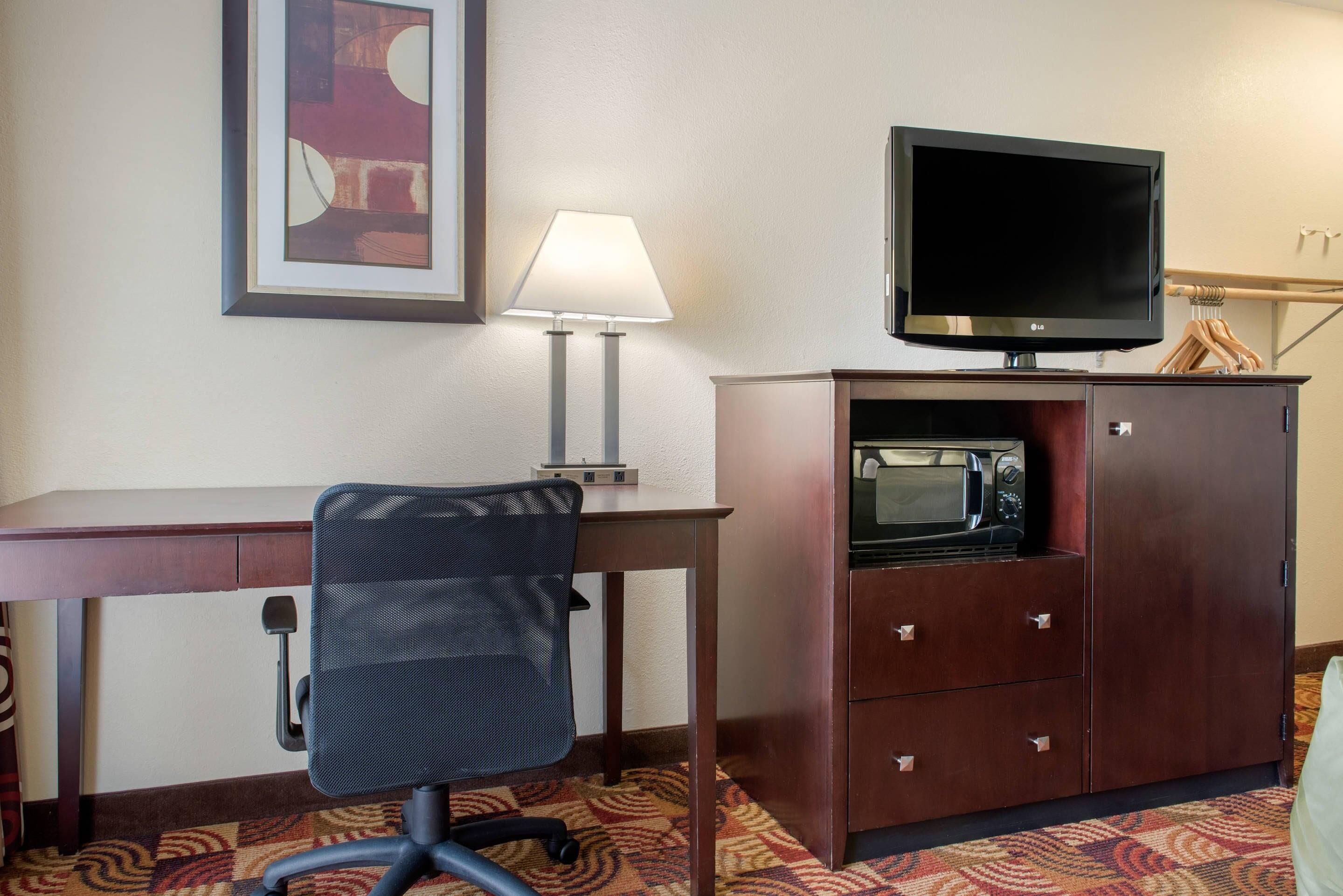 Une chambre d’hôtel équipée d’un bureau, d’un fauteuil de bureau, d’une lampe, d’une télévision, d’un four à micro-ondes et d’un placard.