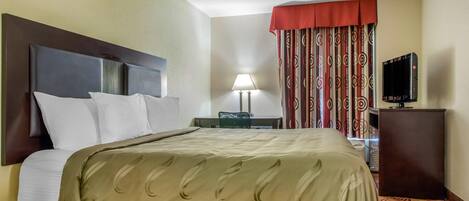 A hotel room with a bed, a desk, a lamp, a TV, and a patterned curtain.
