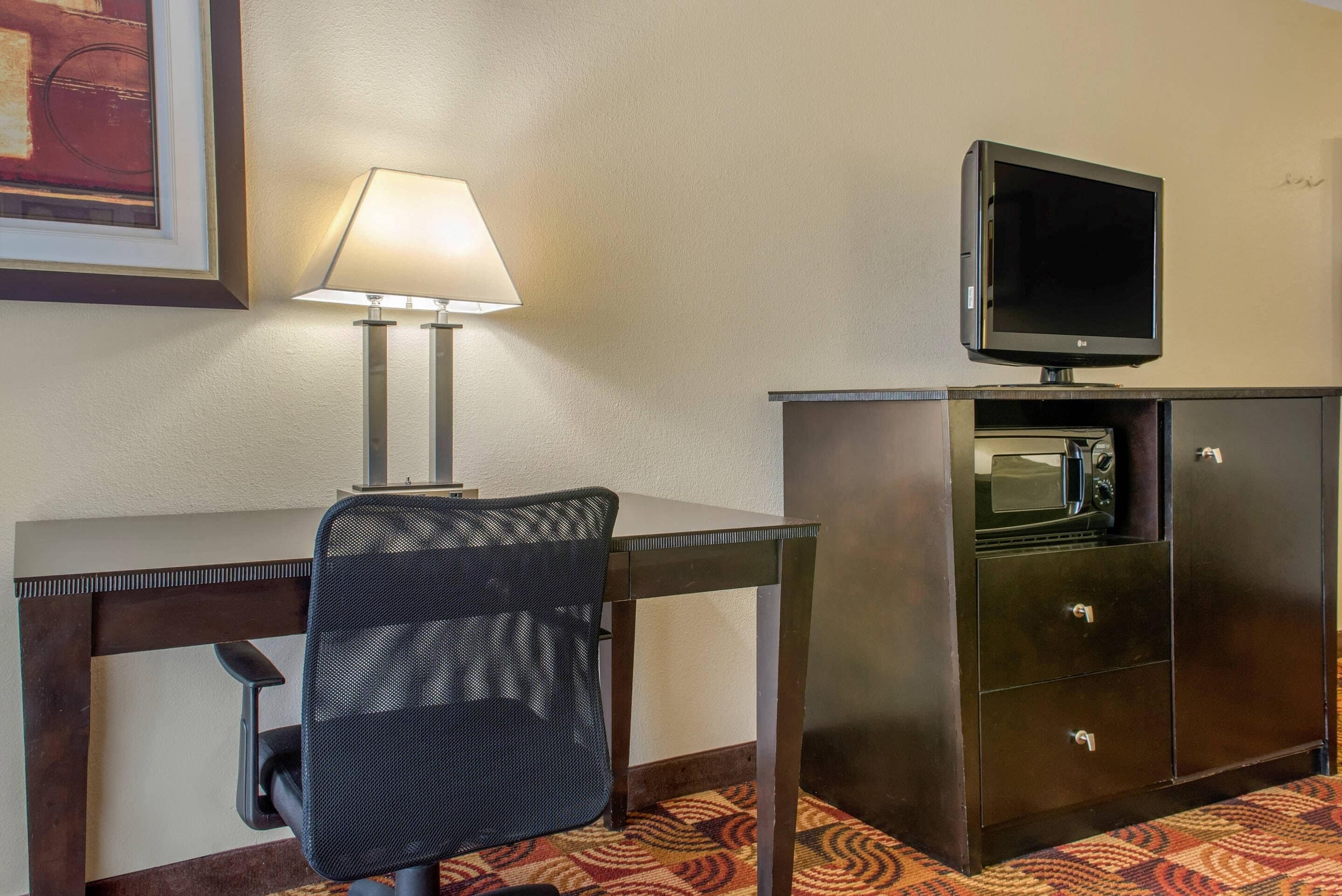 Habitación de hotel con escritorio, silla, lámpara, televisor y microondas.
