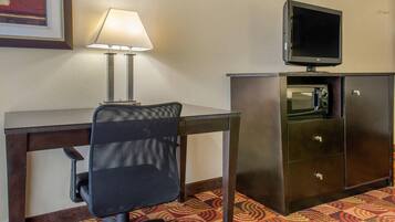Habitación de hotel con escritorio, silla, lámpara, televisor y microondas.