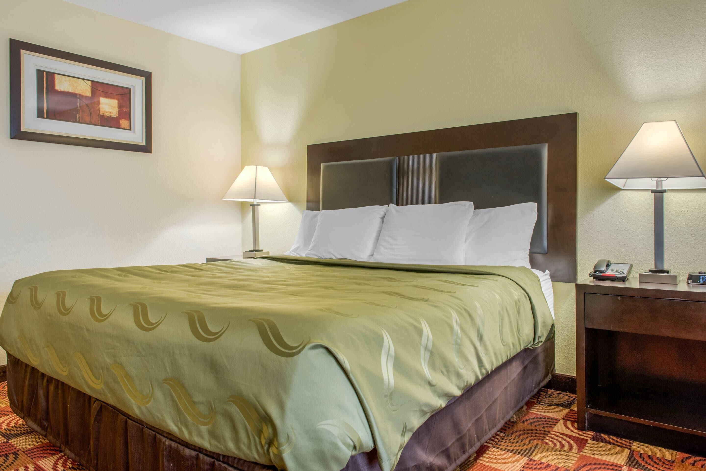 Una habitación de hotel con una cama, dos lámparas de noche, una mesita de noche y un cuadro en la pared.
