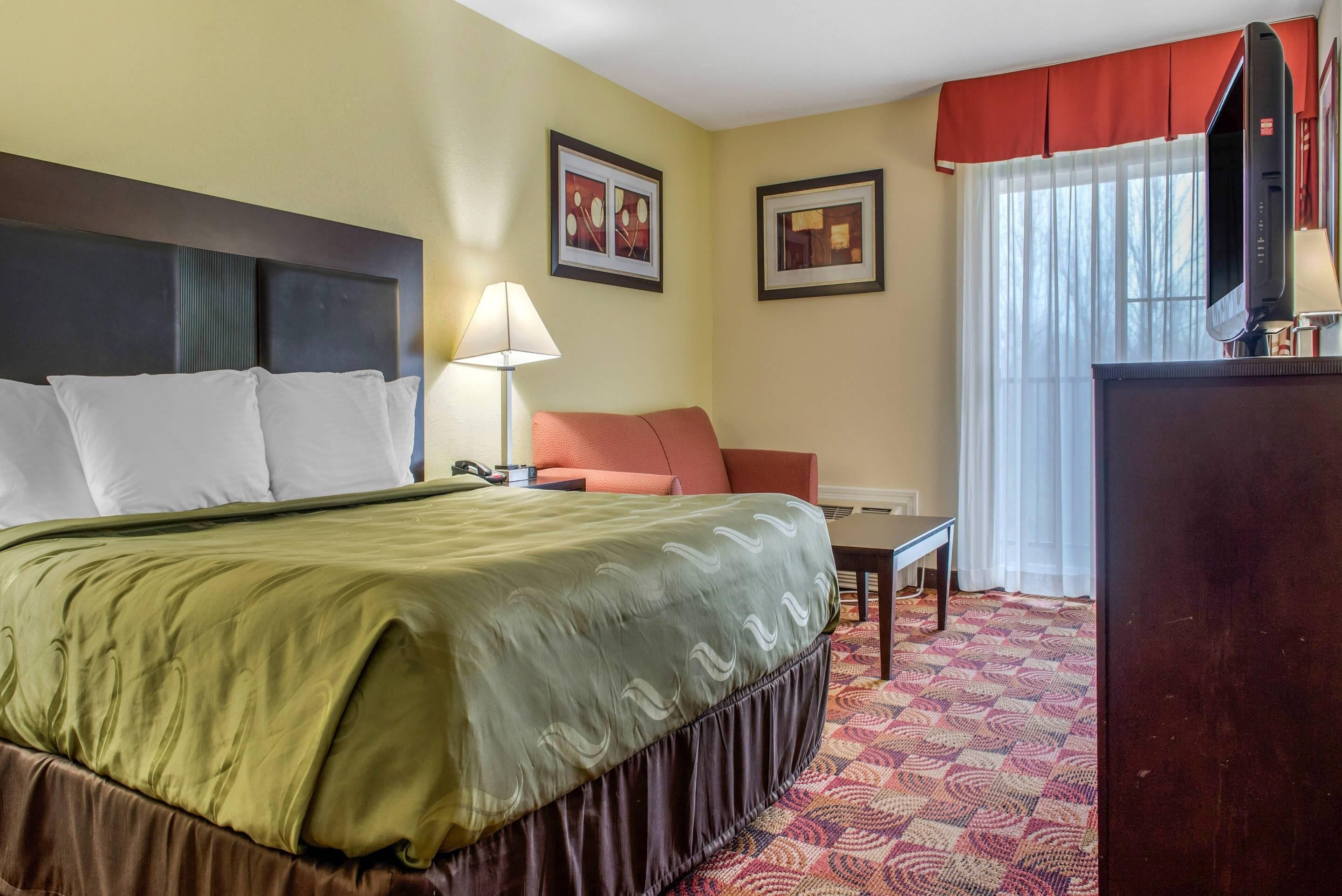 A hotel room with a bed, a desk, a chair, a TV, and a window with curtains.