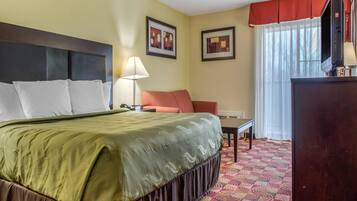 A hotel room with a bed, a desk, a chair, a TV, and a window with curtains.
