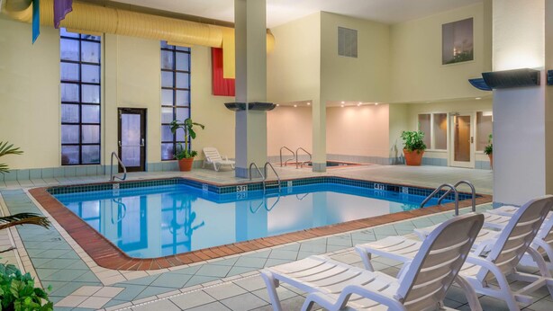 Una piscina interior con agua cristalina, rodeada de sillas reclinables blancas y plantas en macetas.