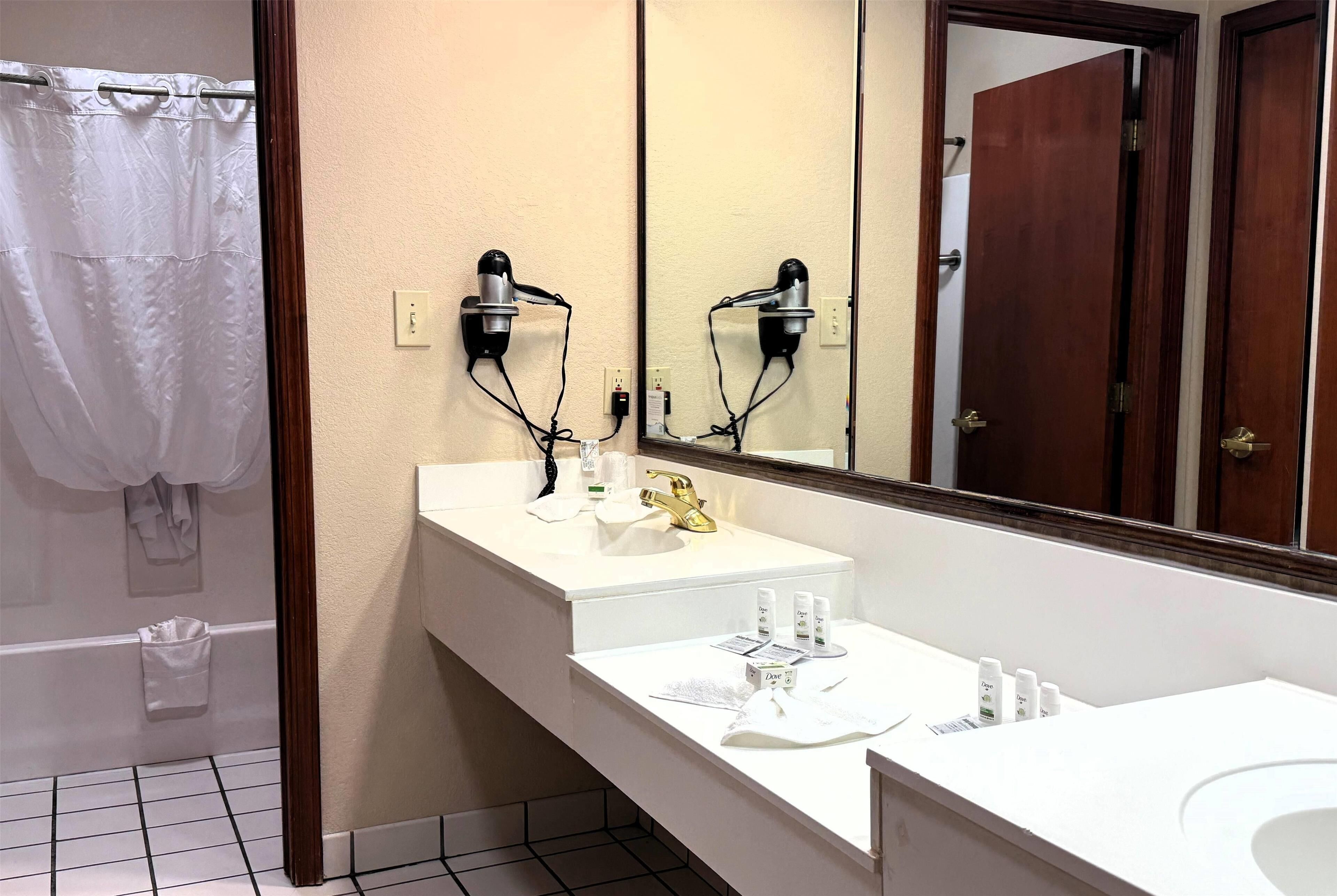 A bathroom with a white sink, a gold faucet, a mirror, and two hair dryers mounted on the wall.