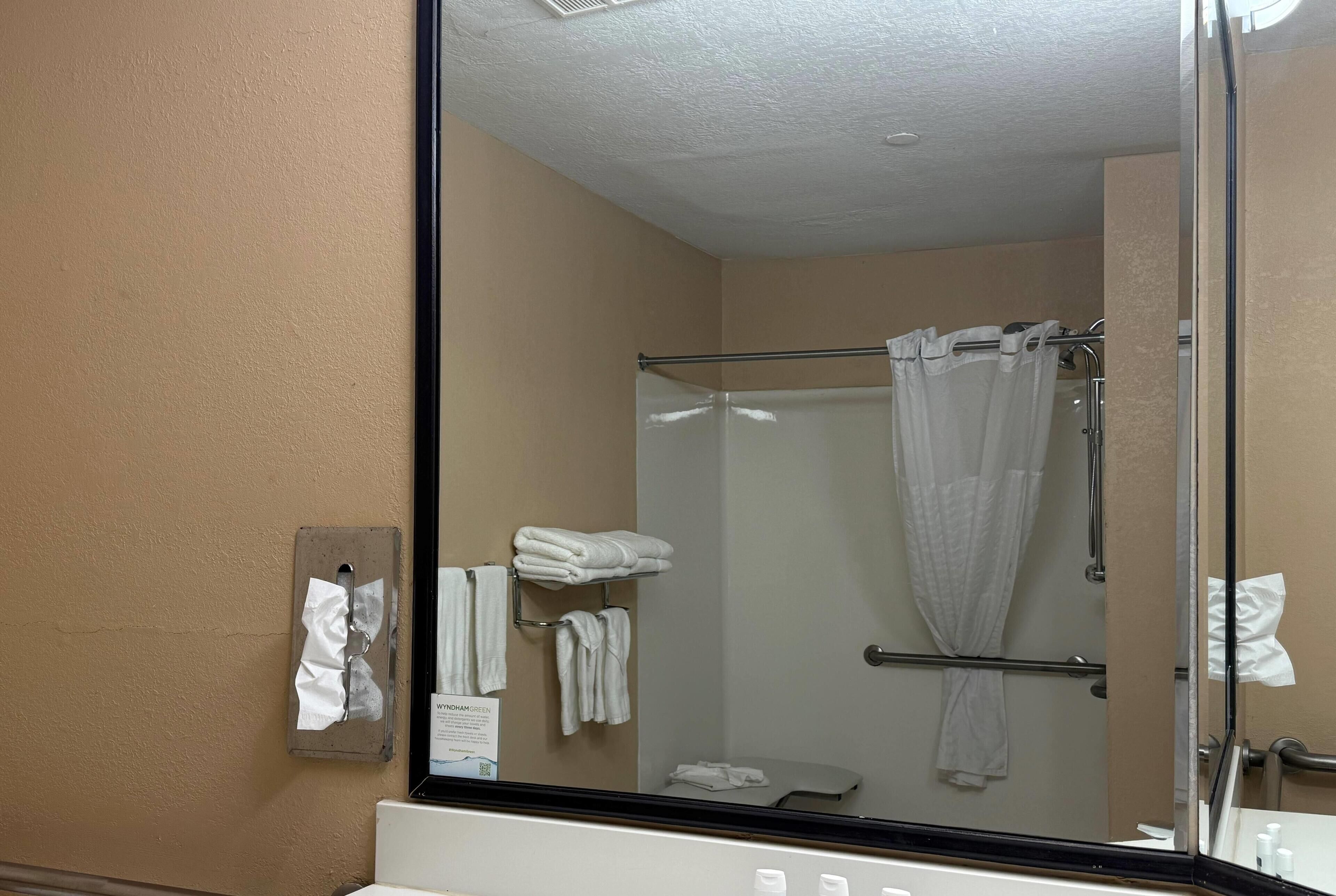 A bathroom with a glass shower enclosure, a towel rack with folded towels, and a paper towel dispenser.