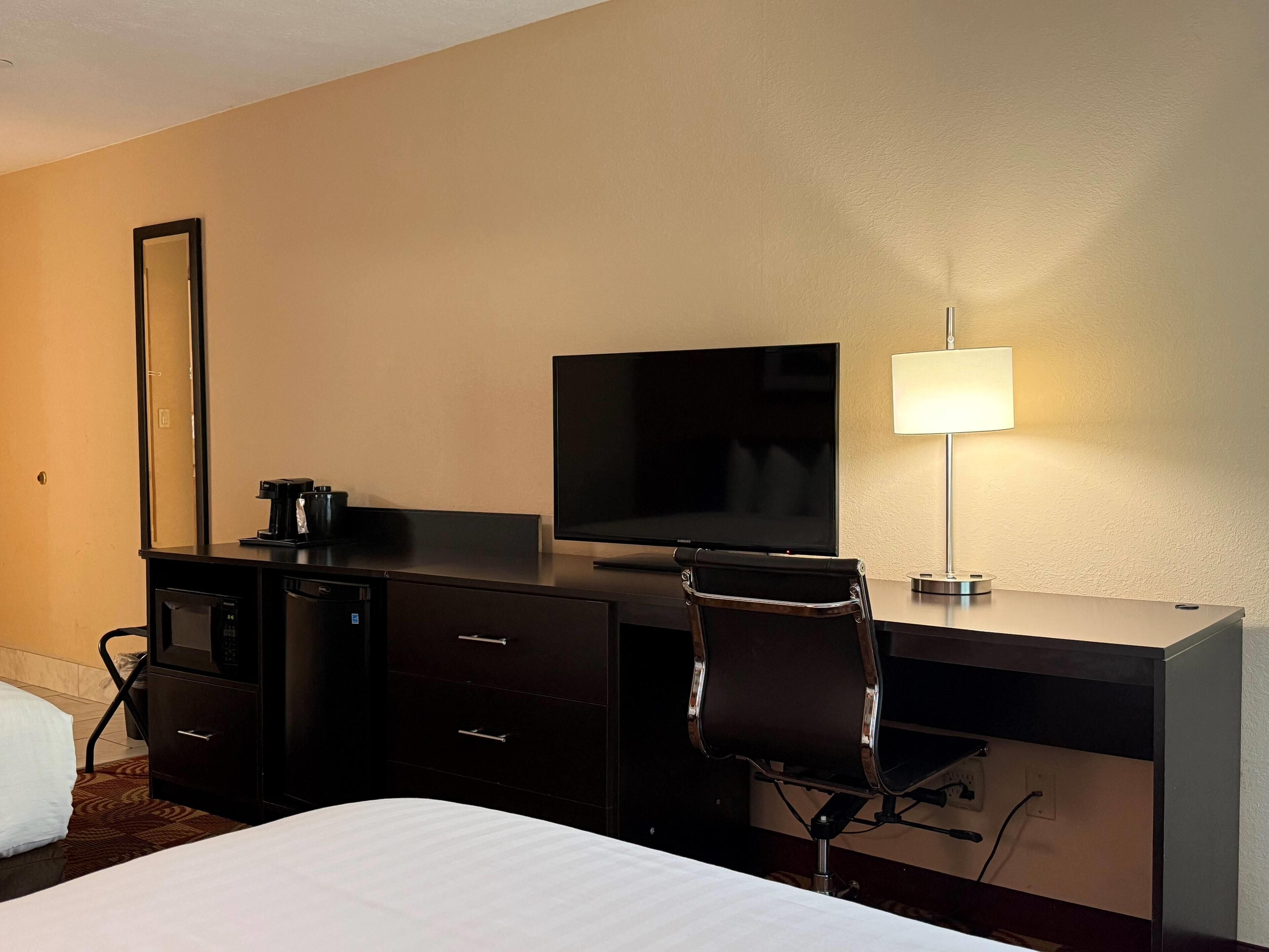 A hotel room with a bed, a desk with a flat-screen TV, a lamp, and a chair.