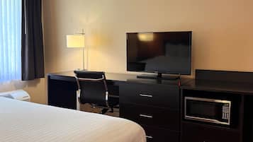 A hotel room with a bed, a desk with a chair, a television, a lamp, a microwave, and a small safe.