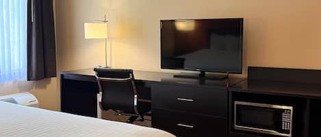 Hotelkamer met een bed, bureau met stoel, televisie, lamp, magnetron en een klein kluisje.