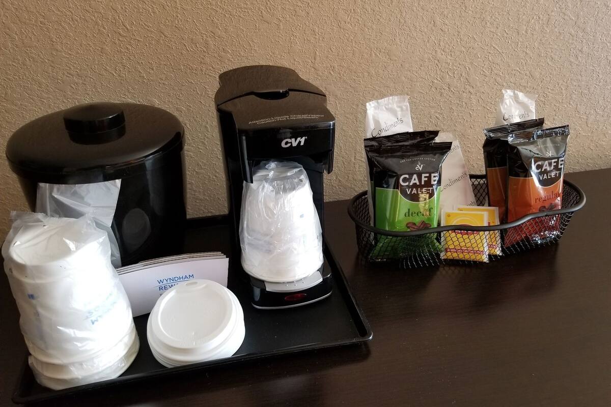 Una estación de café con cafetera, vasos desechables y cápsulas de café.